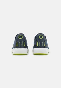 Zapatillas deportivas azules con un upper texturizado, suelas blancas y acentos verdes. Presentan una lengüeta circular en el talón y un detalle de costura en zig-zag.