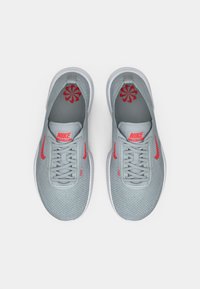 Nike Free tenisice u svijetlosivoj mrežastoj tkanini s crvenim detaljima. Značajke uključuju vezice, logo i uzorak unutrašnjeg obloga. Teksturirana gumena potplat.