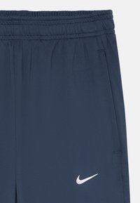 Pantalons de sport bleu foncé avec une taille élastique et des poches latérales. Présente un petit logo Nike blanc en bas à gauche.
