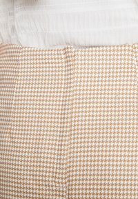 Hnědo-bílá látka s houndstooth vzorem, která má texturovaný svrchní materiál. Disponuje hladkým, světlým páskem.
