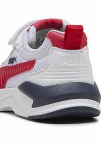 Baskets Puma blanches et rouges avec un dessus en mesh, une semelle intermédiaire bleue marine, une languette rouge et une sangle Velcro, vues de l'arrière et de côté.