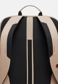 Zaino con design marrone e nero, dotato di spallacci imbottiti e pannello posteriore testurizzato. Include una maniglia superiore e dettagli decorativi.