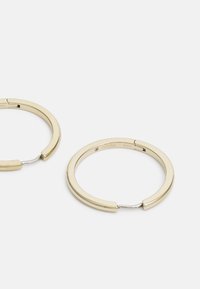 Ohrringe aus goldfarbenem Edelstahl mit glattem, abgerundetem Design und Klappverschluss. Minimalistisch mit glänzender Oberfläche und dezenter Markierung.