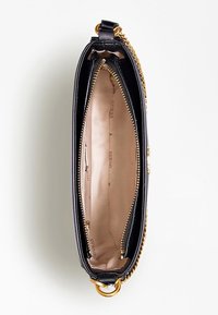 Sort lædertaske med guldkæde som accent. Lynlåslukning, der åbner til beige indre med mærkning og rum. Glat tekstur, slankt design.