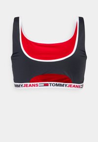 Desporto preto e vermelho com decote em forma de scoop, acabamento branco e uma banda elástica com a marca "TOMMY JEANS" em letras grandes.