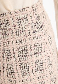 Roze en crèmekleurige geweven stof met een gemêleerd, geruit patroon en metallic draad. De stof heeft een zachte, donzige uitstraling.