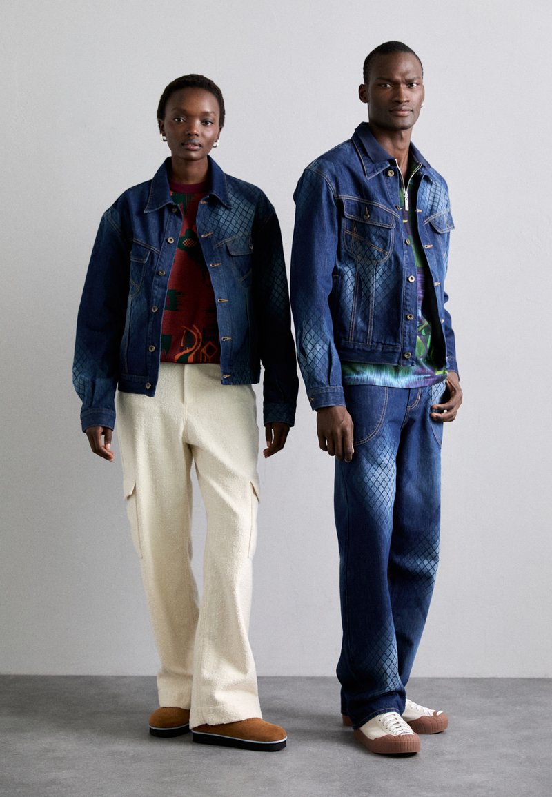 Twee modellen dragen spijkerjacks met gestructureerde patronen, gecombineerd met kleurrijke shirts, crèmekleurige cargo-broeken en contrasterende schoenen.