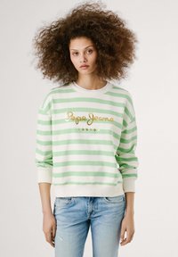 Pullover a righe verdi e bianche con colletto a girocollo, con testo dorato "Pepe Jeans London". Indossato con jeans in denim azzurro chiaro.