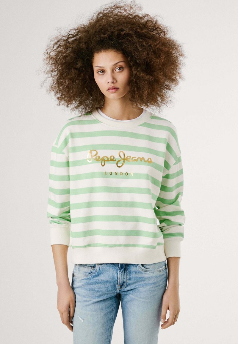 Pullover a righe verdi e bianche con colletto a girocollo, con testo dorato "Pepe Jeans London". Indossato con jeans in denim azzurro chiaro.