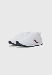 Scarpe da ginnastica bianche in mesh traspirante, con un design texture, suola in gomma scura e un accento a strisce rosse e blu.