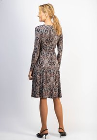 Mekko pitkähihaisena tummasta kankaasta, jossa on punaisista, beigeistä ja mustista paisley-kuvioista; vyötäröltä napakka, hameosa levenee, yhdistetty mustiin korkokenkiin.