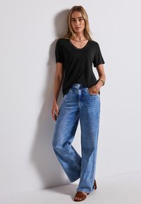 Černé tričko s krátkým rukávem a výstřihem do V s jemným detailem, spárované s světle modrými širokými džínami a hnědými sandály.