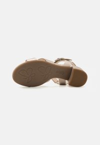Sandal beige chiaro con suola texturizzata. Presenta una fascia regolabile e una tomaia liscia simile alla pelle. Motivo floreale impresso sulla suola.