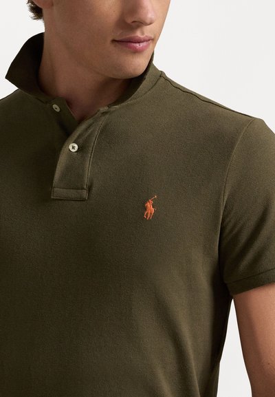 Olive roheline polo särk, mis on valmistatud tekstuurilisest kangast, millel on nööpidega krae ja vasakul rinnal oranž tikitud logo.