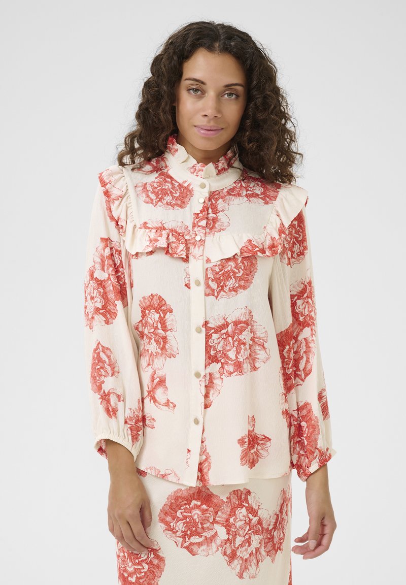 Floral blouse featuring a cream background with red flower prints, ruffled collar, button front, and long sleeves with elastic cuffs.