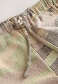 Tkanina we wzór kamuflażu w odcieniach zieleni, brązu i szarości. Elastyczna talia z wiązanym sznurkiem ozdobnym. Miękka tekstura.