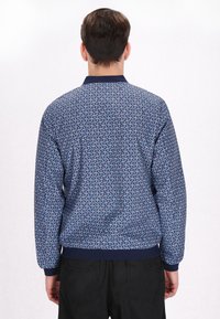 Marineblaue Bomberjacke mit einem gemusterten Stoff und kleinen floralen Designs, gerippten Bündchen und einem Bund, von hinten betrachtet.