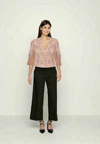 Blusa rosa com um decote em V profundo e bordados florais, combinada com calças largas pretas e saltos altos pretos com tiras. Texturas suaves.