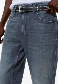 Mörkblå denimjeans med en slät textur, prydda med ett svart nitarbälte och en silverspänne. Rak bendesign med klassiska fickor.