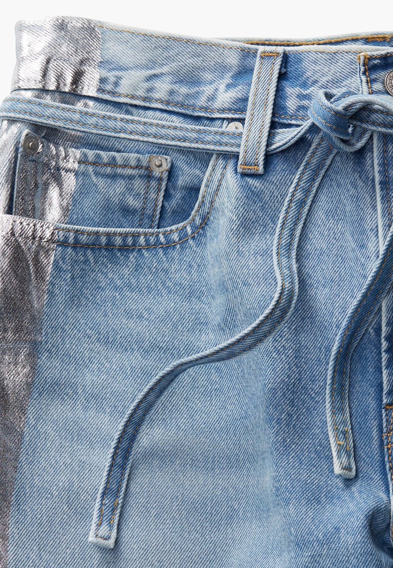 Shorts di denim azzurro chiaro con pannello laterale metallico argento, caratterizzati da una vita legata, passanti per cintura e cuciture a contrasto.