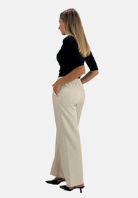 Pantaloni beige a gamba larga con vita elastica, tasche laterali, abbinati a un top nero aderente e scarpe con tacco nere.