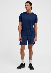 Navy sportshirt en shorts van lichtgewicht materiaal. Het shirt heeft een klein logo op de borst en de shorts hebben zijzakken.