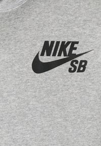 Sudadera gris hecha de una mezcla de algodón con un logo negro de Nike y el texto "SB" impresos en el pecho. Textura suave, diseño de cuello redondo estándar.