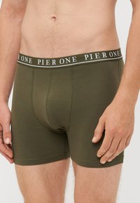 Boxer-briefs vert olive à coupe ajustée. Dotés d'une taille noire avec le logo "PIER ONE" en blanc. Fabriqués en matériau doux et extensible.
