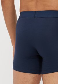 Marineblå boxertruser laget av glatt stoff, med en myk midjebånd og minimal søm, med en tettsittende design.