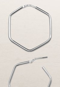 Sechseckiger Silber-Sonnenbrillenrahmen mit polierter Metalloberfläche, ausgestattet mit einem Scharniere- und Bügeldesign, vor einem hellen Holz-Hintergrund präsentiert.