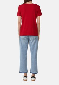 Rood katoenen T-shirt met ronde hals, gecombineerd met lichtblauwe wijde jeans met een omgeslagen zoom en subtiele steekjes op de achterzak.