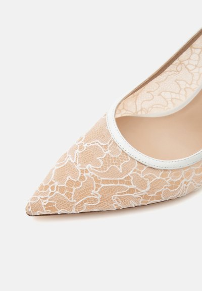 Chaussure beige à bout pointu avec une superposition de dentelle florale blanche et un bord blanc autour de l’ouverture.