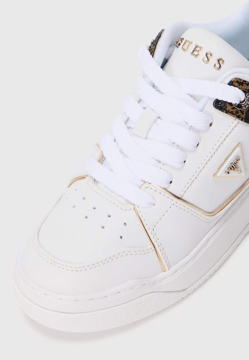 Witte Guess sneakers met dikke witte veters, gouden accenten, perforaties op de tenen en een driehoekig Guess-logo op de zijkant.