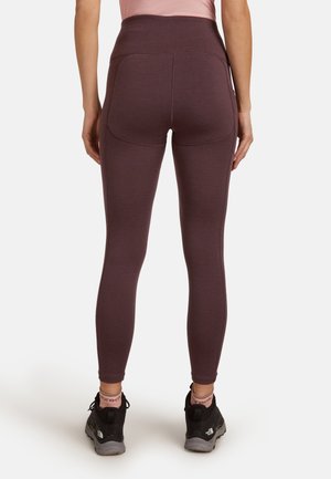 Leggings taille haute bordeaux avec une texture lisse, dotés de poches latérales et d'un design ajusté. Portés avec des chaussures noires et des chaussettes roses.