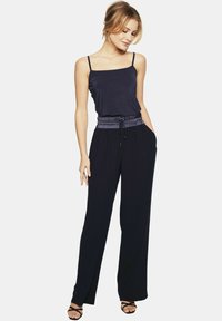 Granatowy kombinezon z dopasowanym topem, regulowanymi ramiączkami i elastycznym pasem. Szerokie nogawki z kieszeniami bocznymi i gładką fakturą.