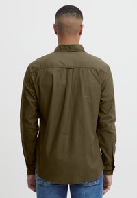 Olive zelena longsleeve srajca z ovratnikom na gumb, detajli na hrbtni strani in nastavljivimi manžetami. Zaključena je v mehkem, teksturiranem materialu.