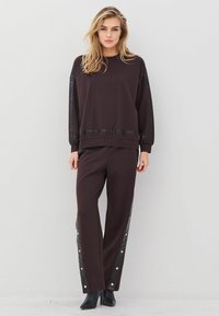 Tumepruun sweatshirt läikiva musta külgpaneeliga, vastavad püksid, millel on näppide aktsendid sääre peal. Mustad kontsakingad. Lihtne disain.