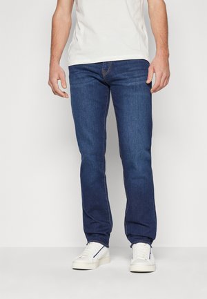 Dunkelblaue Jeans mit geradem Bein, ausgestattet mit orangefarbenen Nähten und einem klassischen Fünf-Taschen-Design, kombiniert mit weißen Sneakern.