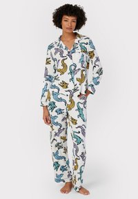 Vitt pyjamas-set med färgglada mönster av alligatorer i blått, gult och lila. Mjukt tyg, långa ärmar och löst sittande byxor.