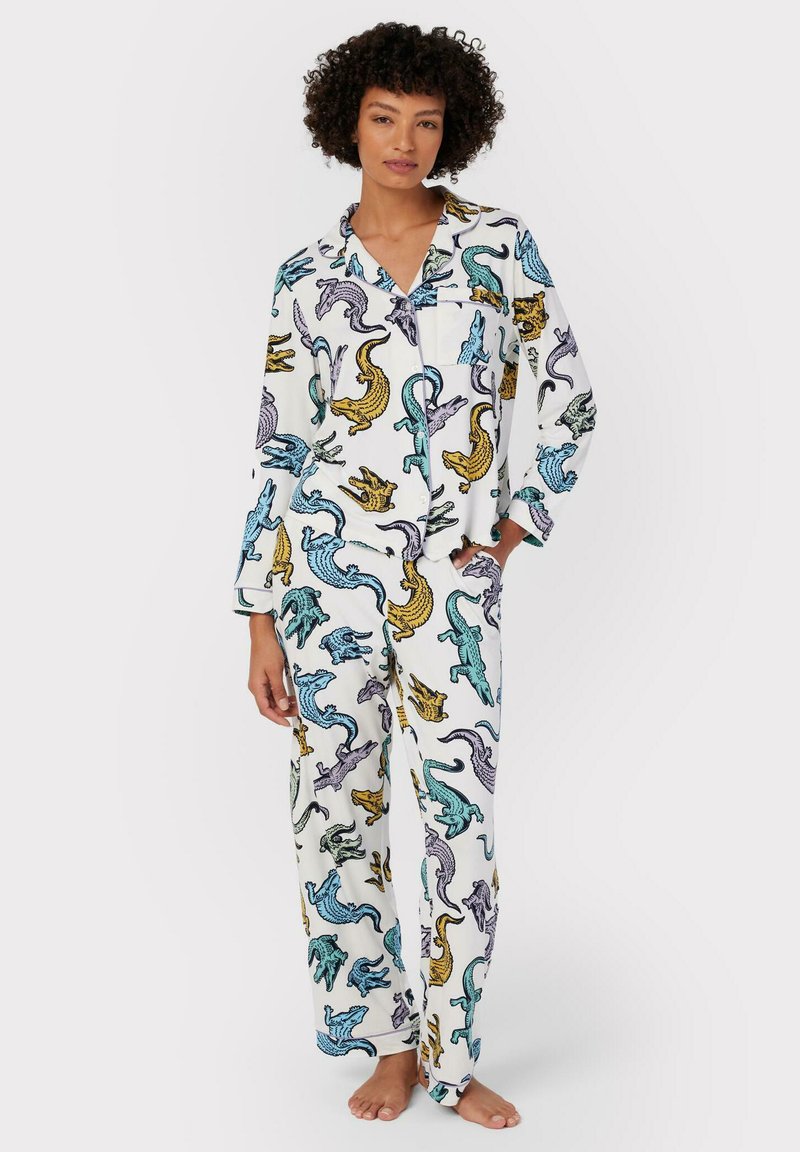 Vitt pyjamas-set med färgglada mönster av alligatorer i blått, gult och lila. Mjukt tyg, långa ärmar och löst sittande byxor.