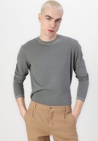 Gray long-sleeve shirt with a round neck and cuffed sleeves, paired with tan trousers featuring a front button. Smooth fabric texture.