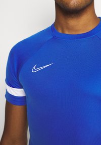 Blue athletic T-shirt with short sleeves, featuring a white Nike logo and a white stripe on the sleeve, made from a smooth, stretchy material.
