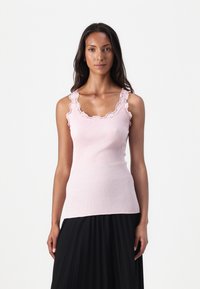 Débardeur rose clair à côtes avec un col en dentelle festonné, design ajusté et fines bretelles, associé à une jupe noire plissée.