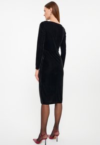 Schwarzes Samtkleid mit langen Ärmeln, tailliertem Oberteil und knielangem Saum. Bemerkenswert für seine glatte Textur und den subtilen Glanz.
