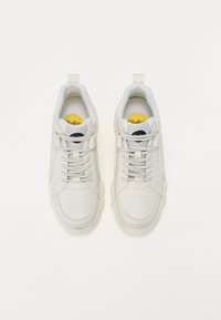 Balti odiniai sportbačiai su lygiu paviršiumi, turintys šviesiai pilkas raišteles, paminkštintą apykaklę ir apvalų juodą logotipą ant liežuvėlio.