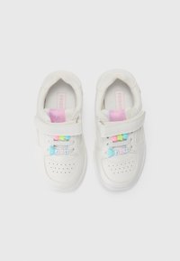 Une paire de baskets blanches pour enfants avec des semelles intérieures roses, des bandes Velcro, et des perles colorées écrivant "JOIE" sur les lacets.