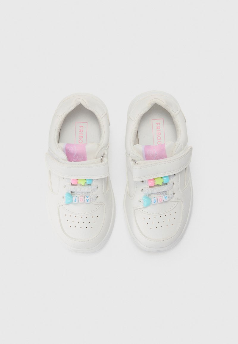 Une paire de baskets blanches pour enfants avec des semelles intérieures roses, des bandes Velcro, et des perles colorées écrivant "JOIE" sur les lacets.