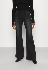 Vaqueros negros de campana con una textura suave, cintura alta, bolsillos frontales y traseros, y un sutil efecto deslavado, combinados con botas de tobillo.