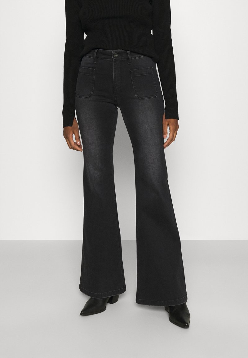 Vaqueros negros de campana con una textura suave, cintura alta, bolsillos frontales y traseros, y un sutil efecto deslavado, combinados con botas de tobillo.