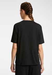 Camiseta negra de manga corta con corte relajado, textura suave y cuello redondo estándar, que presenta un dobladillo recto y detalles de costura.